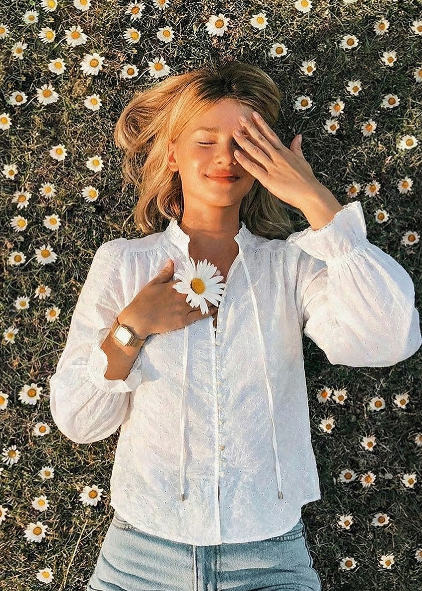 Woman in a white shirt lying among daisies, holding a flower.