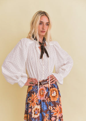 Woman wearing a white blouse and floral skirt against a yellow background