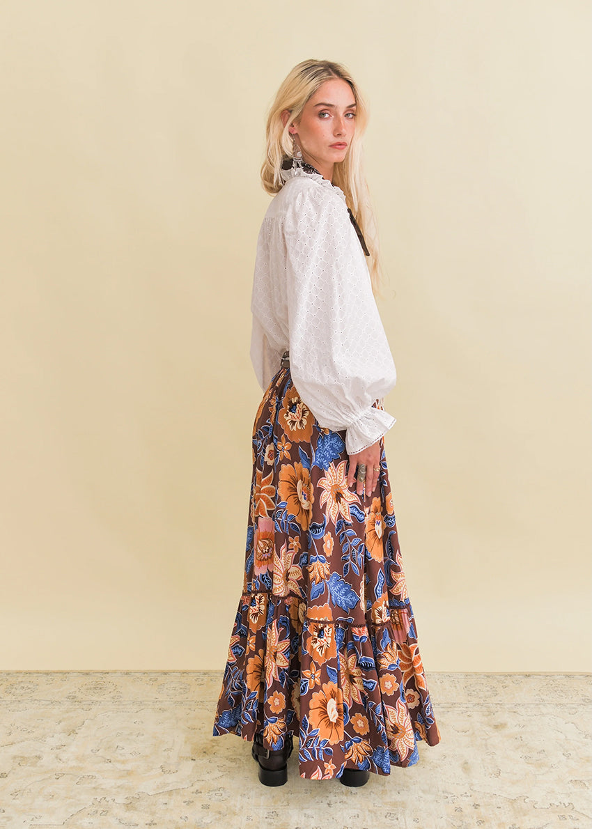 Woman wearing a white blouse and floral skirt against a beige background