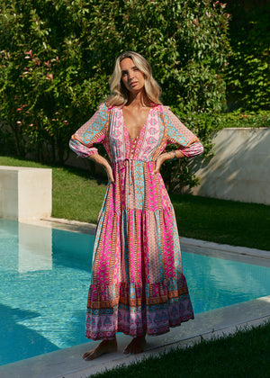 A woman standing by a pool wearing a multicolored floral maxi dress with 3/4 sleeves and V-neckline.