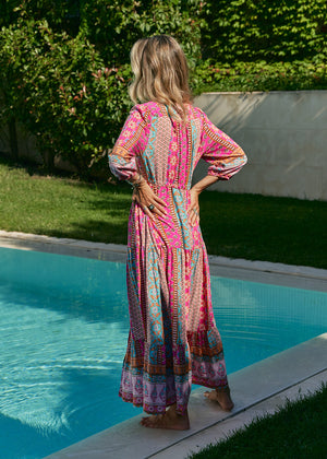 A woman standing by a pool wearing a multicolored floral maxi dress with 3/4 sleeves and V-neckline.