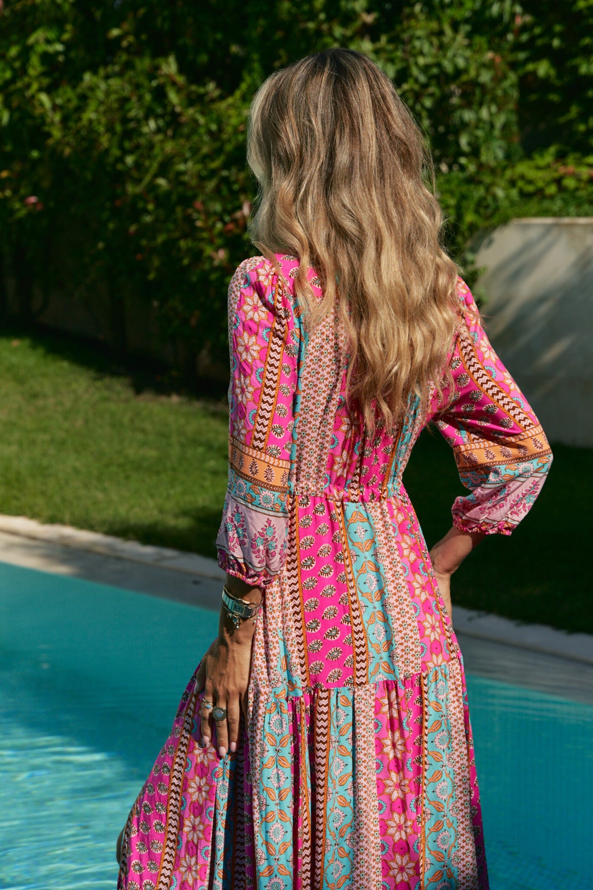 A woman standing by a pool wearing a multicolored floral maxi dress with 3/4 sleeves and V-neckline.