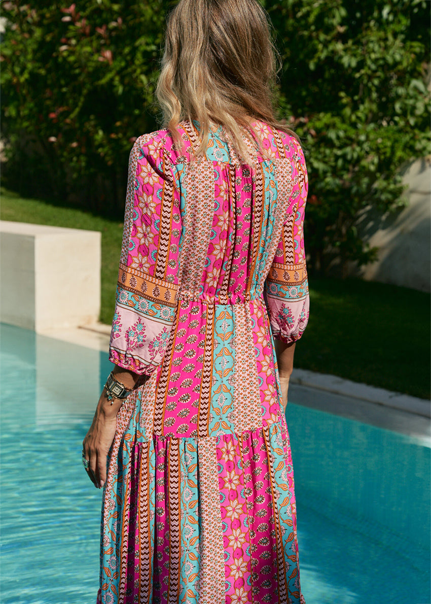 A woman standing by a pool wearing a multicolored floral maxi dress with 3/4 sleeves and V-neckline.