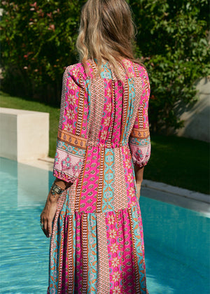 A woman standing by a pool wearing a multicolored floral maxi dress with 3/4 sleeves and V-neckline.