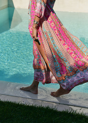 A woman standing by a pool wearing a multicolored floral maxi dress with 3/4 sleeves and V-neckline.