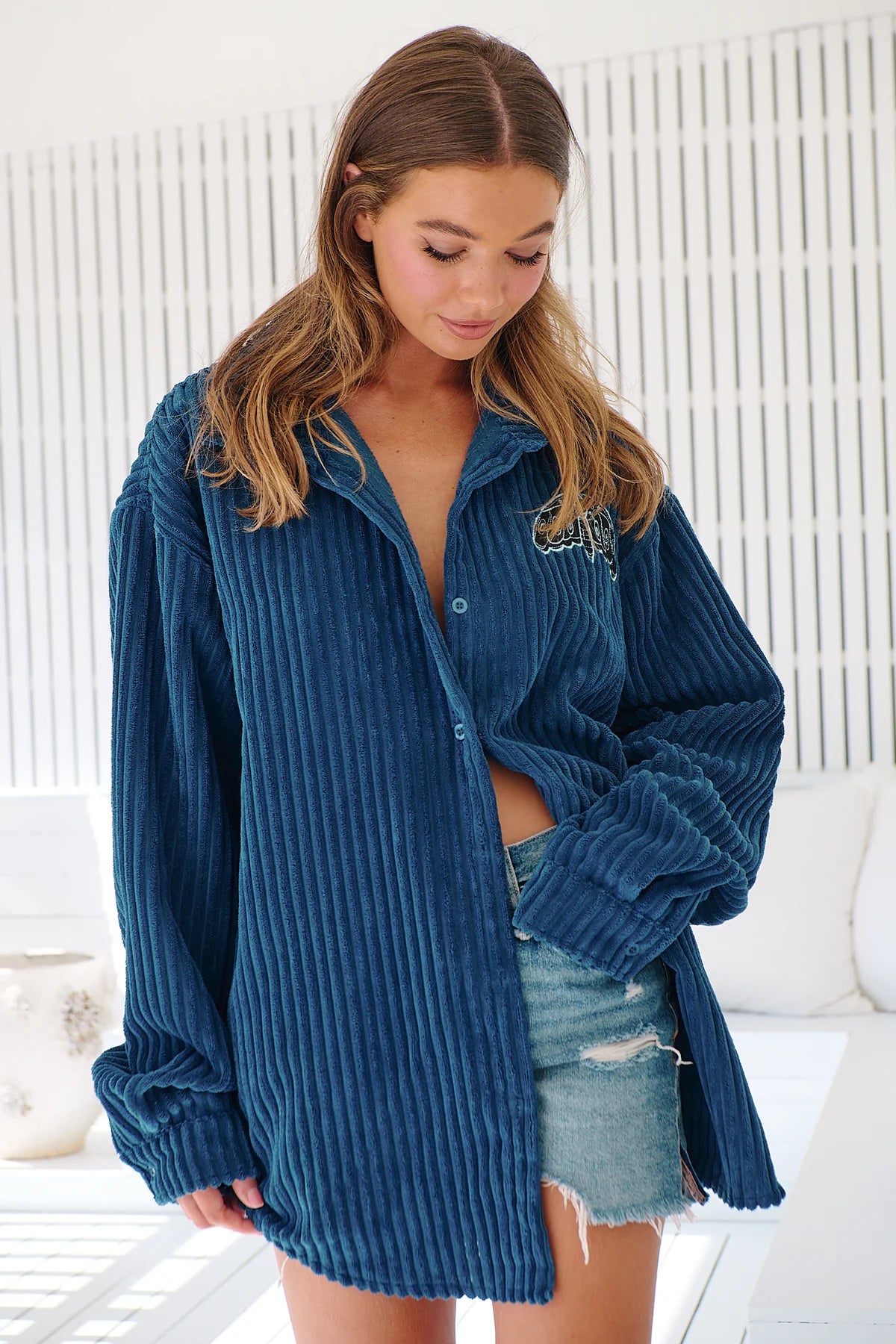 A woman wearing a navy blue corduroy jacket with long sleeves and a button-up front, paired with denim shorts.