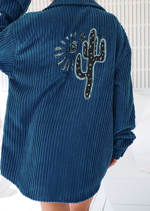 A woman wearing a navy blue corduroy jacket with long sleeves and a button-up front, paired with denim shorts.