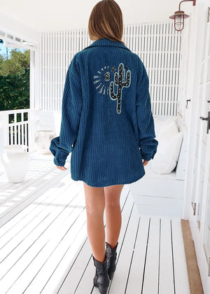 A woman wearing a navy blue corduroy jacket with long sleeves and a button-up front, paired with denim shorts.