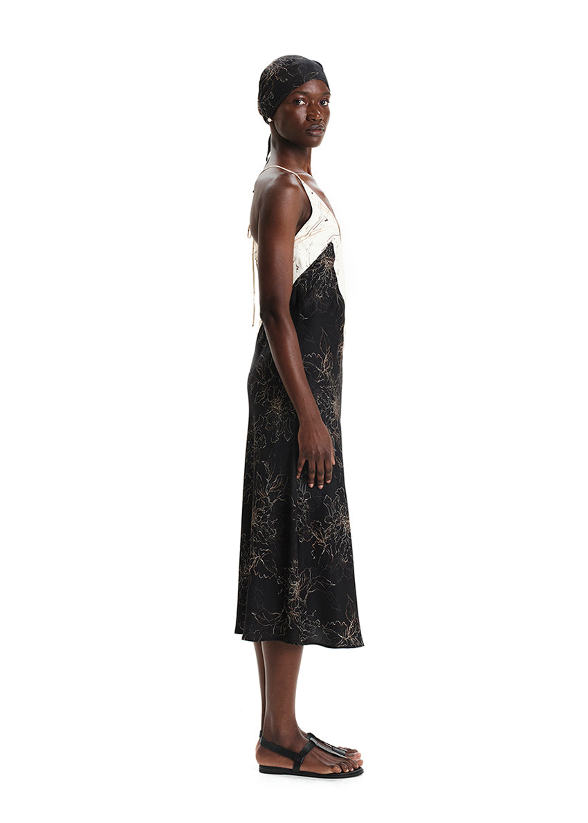 A model wearing a midi-length sleeveless dress with a floral print, a V-neckline, and tie details on the back.