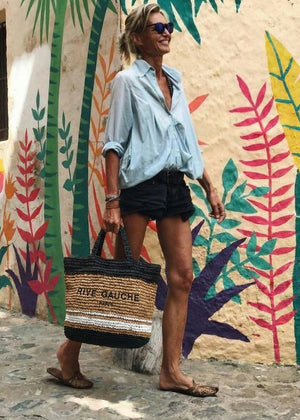 Woman holding a straw bag with a colorful mural in the background