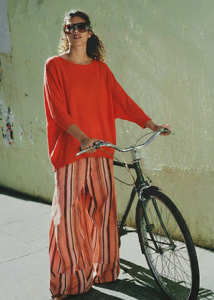 Woman in an orange top and striped pants standing next to a bicycle against a light green wall.