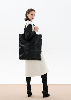 Black tote bag made of artificial leather with shoulder handles and a metallic zipper closure at the top. It features an exterior zipper for size adjustment and an inner pocket with a zipper.