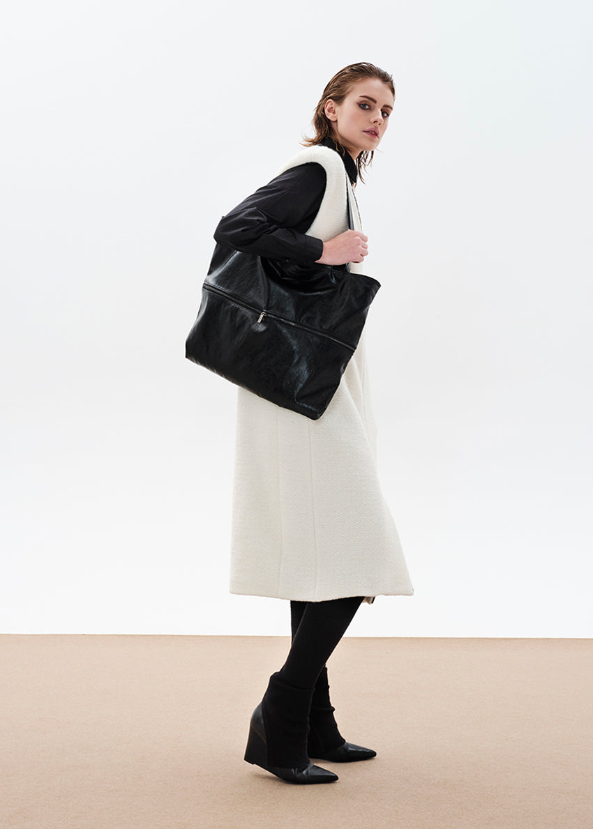 Black tote bag made of artificial leather with shoulder handles and a metallic zipper closure at the top. It features an exterior zipper for size adjustment and an inner pocket with a zipper.