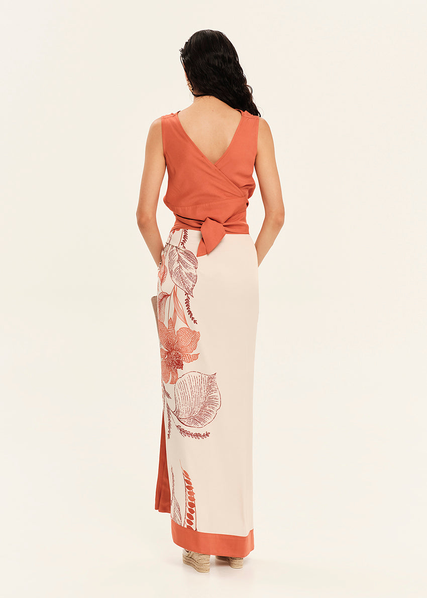 Woman wearing a rust-colored top and white skirt with floral patterns on a white background