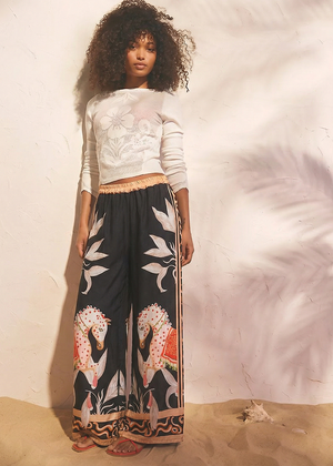 Woman wearing a white top and black patterned pants against a plain background