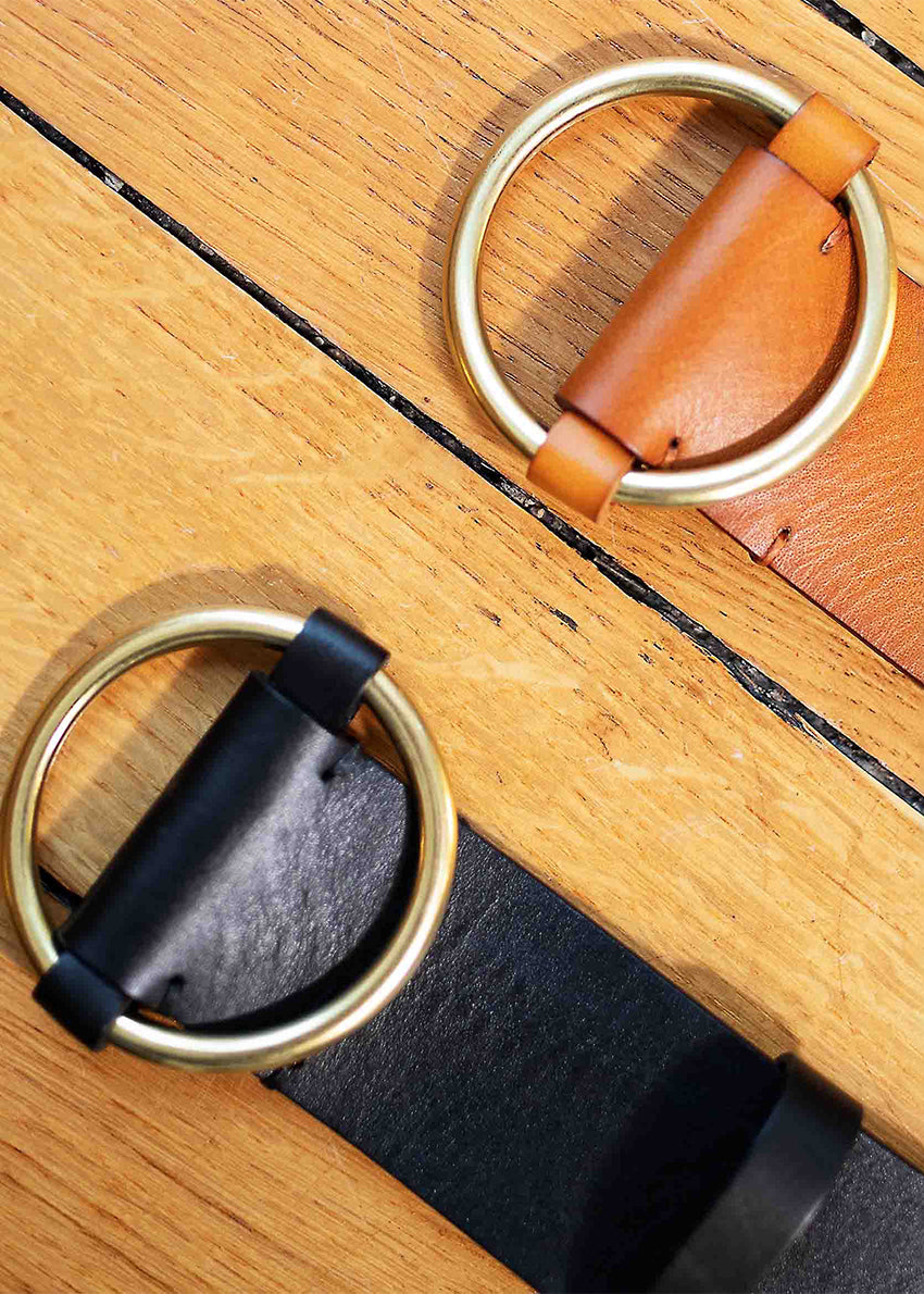 Two leather belts with gold buckles on a wooden surface, one with a dark strap and light buckle, and the other with a light strap and dark buckle.