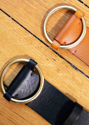 Two leather belts with gold buckles on a wooden surface, one with a dark strap and light buckle, and the other with a light strap and dark buckle.