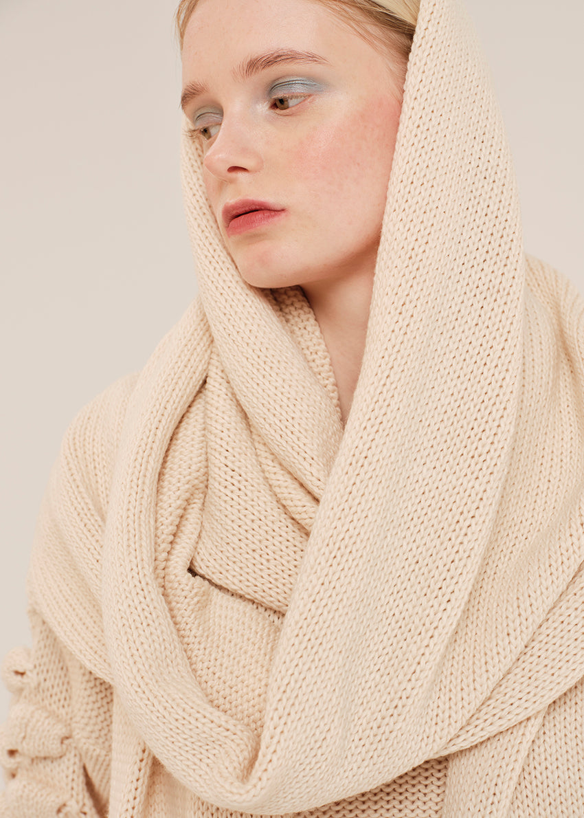 Woman wearing a beige knitted scarf against a plain background