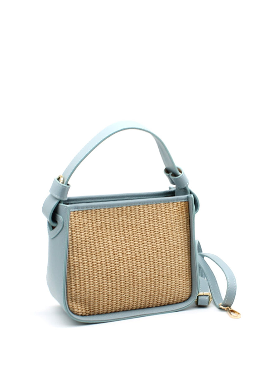 A sky-blue handbag with a natural woven panel and leather accents, featuring an adjustable strap and sturdy handle.