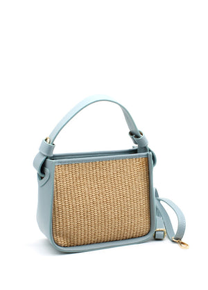 A sky-blue handbag with a natural woven panel and leather accents, featuring an adjustable strap and sturdy handle.