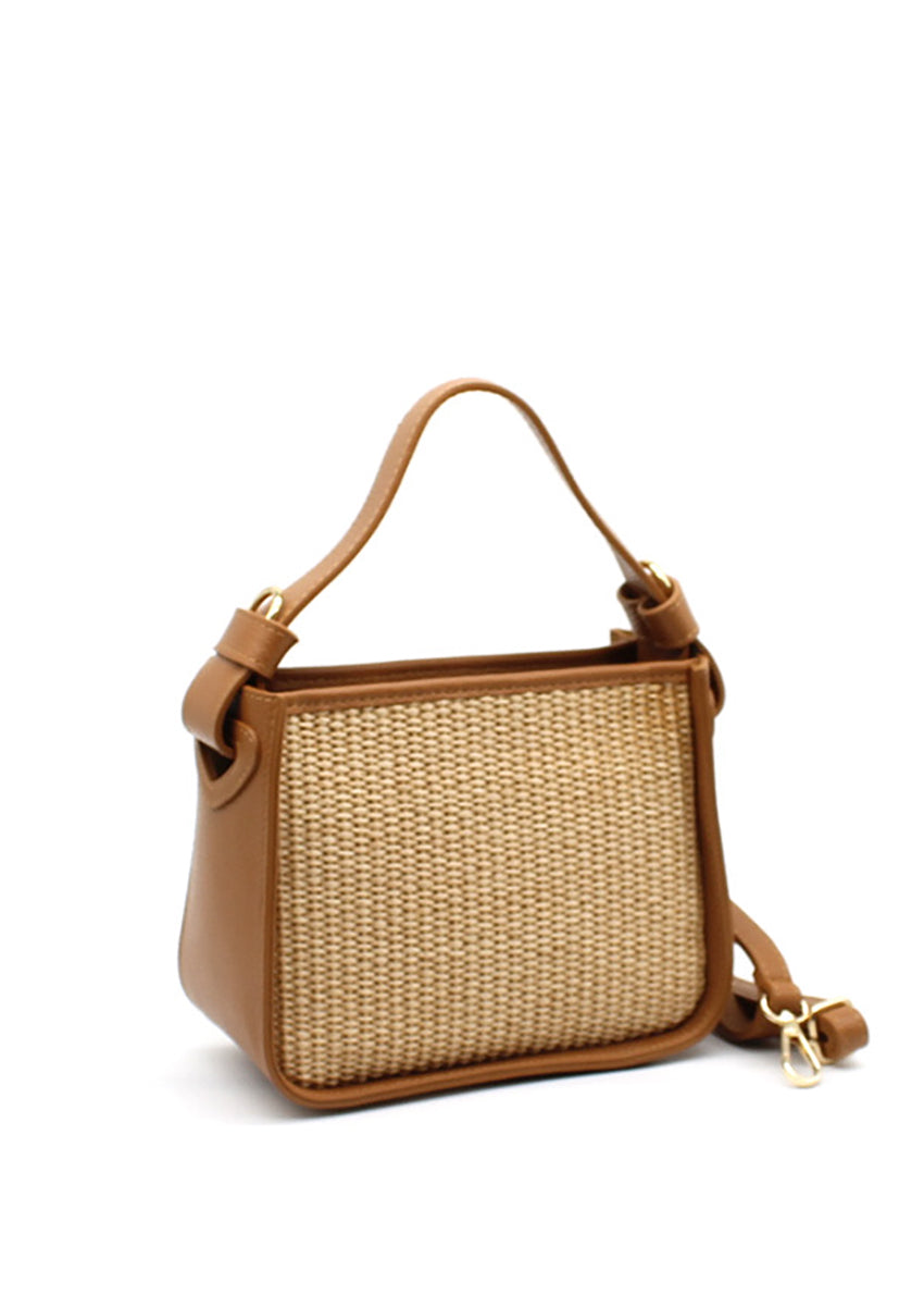 A brown handbag with a natural woven panel and leather accents, featuring an adjustable strap and sturdy handle.