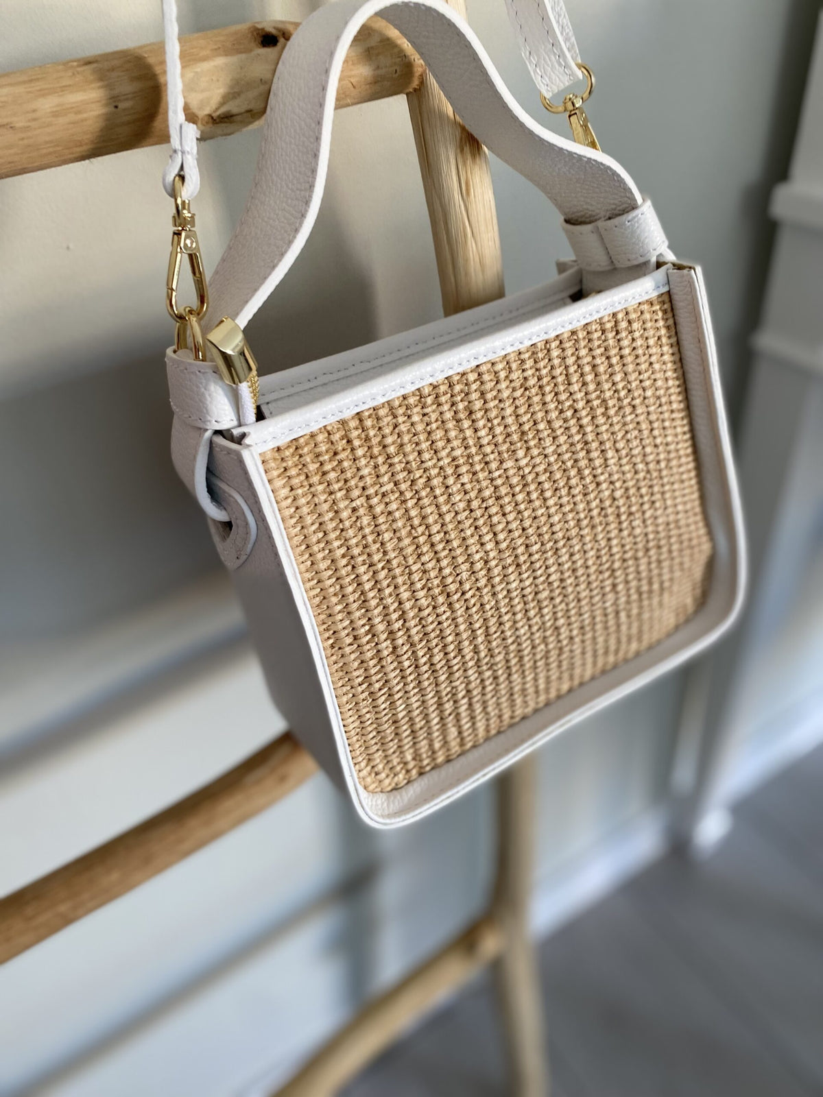 Handbag with woven front panel and beige strap on a wooden surface