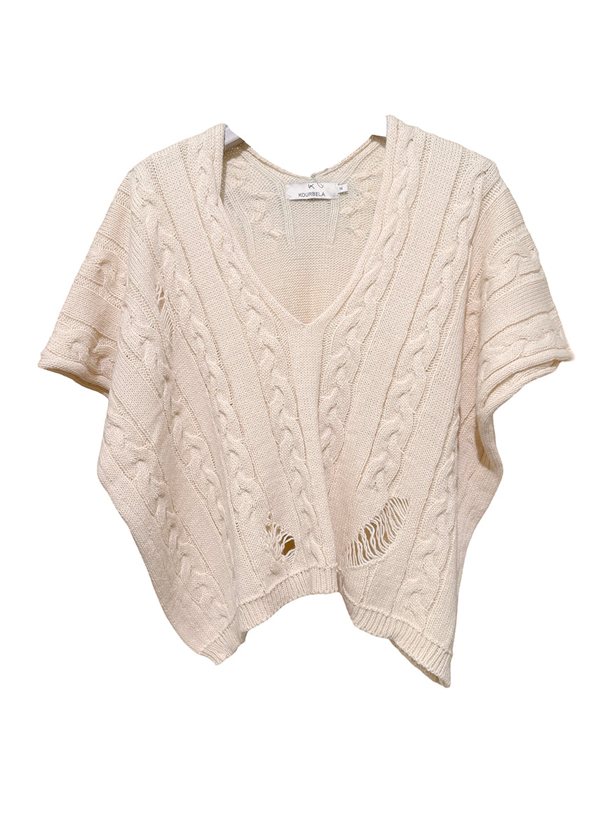 Person wearing a brown cable knit vest over a white shirt with beige pants on a white background