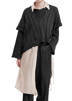 Person wearing a dark gray cable knit sweater over a light shirt with black pants on a white background