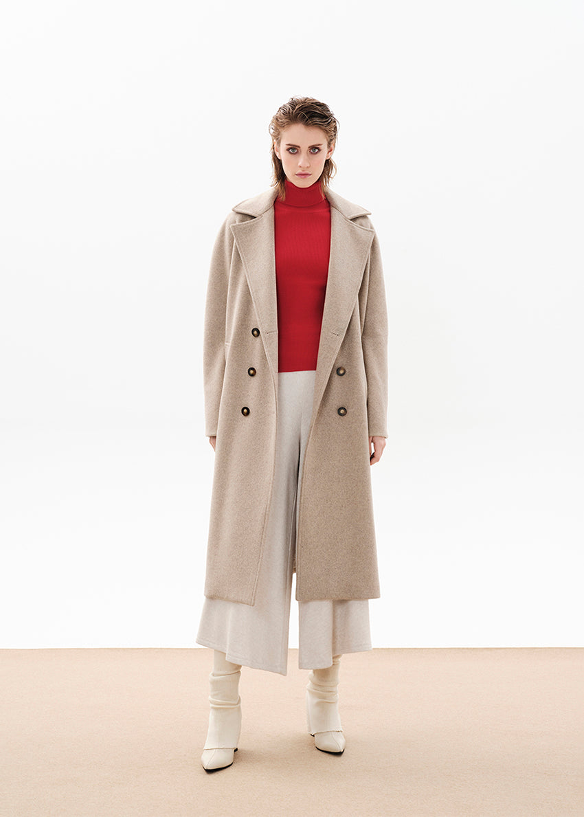 Person wearing a beige wool coat with a red sweater and white pants on a white background 