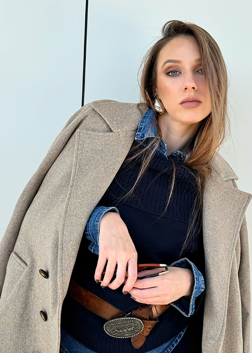 Person wearing a beige wool coat with a black dress and brown boots