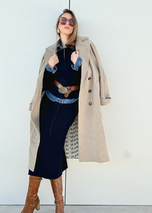 Person wearing a beige wool coat with a black dress and brown boots