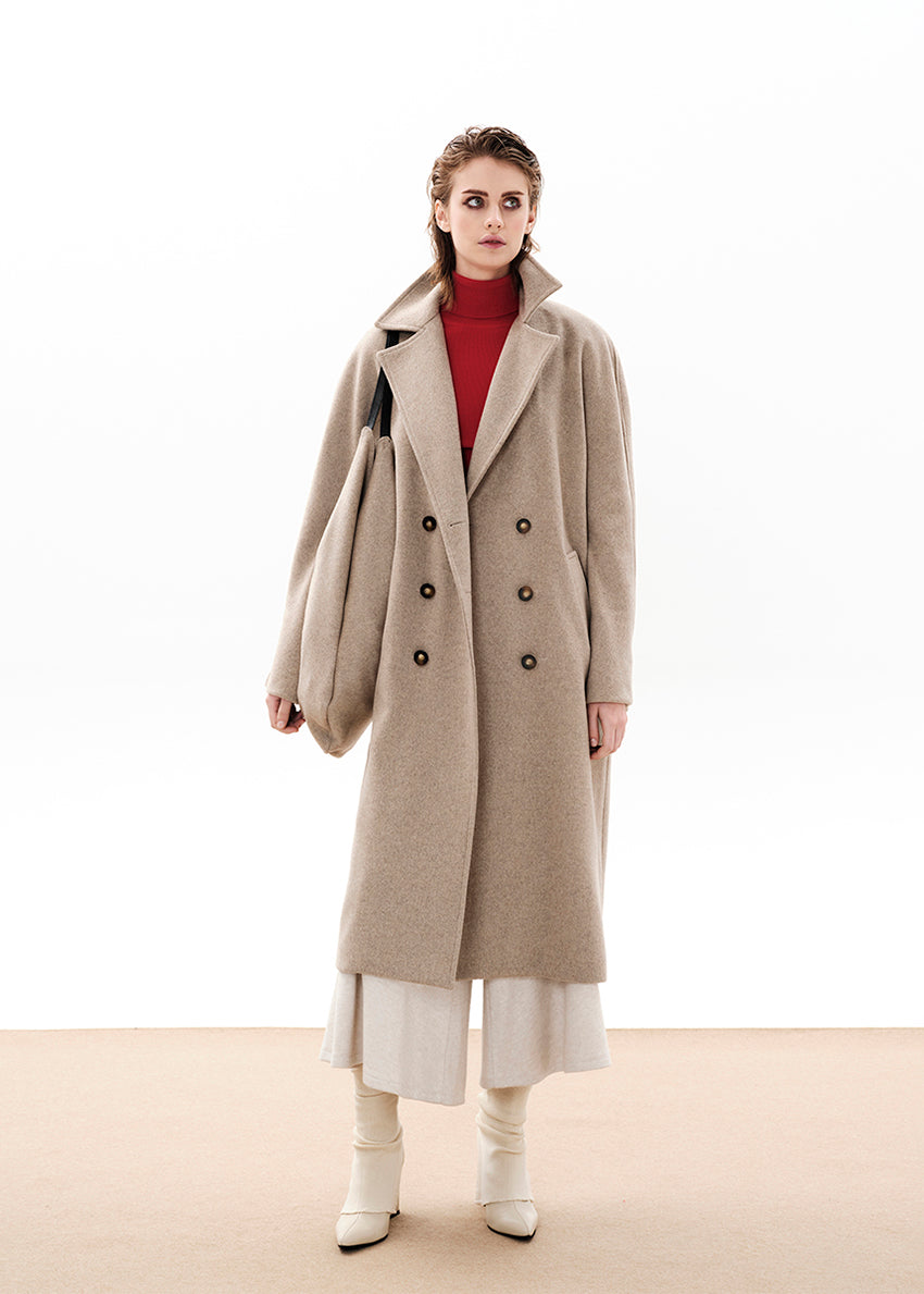 Person wearing a beige wool coat with a matching bag and white pants on a white background 