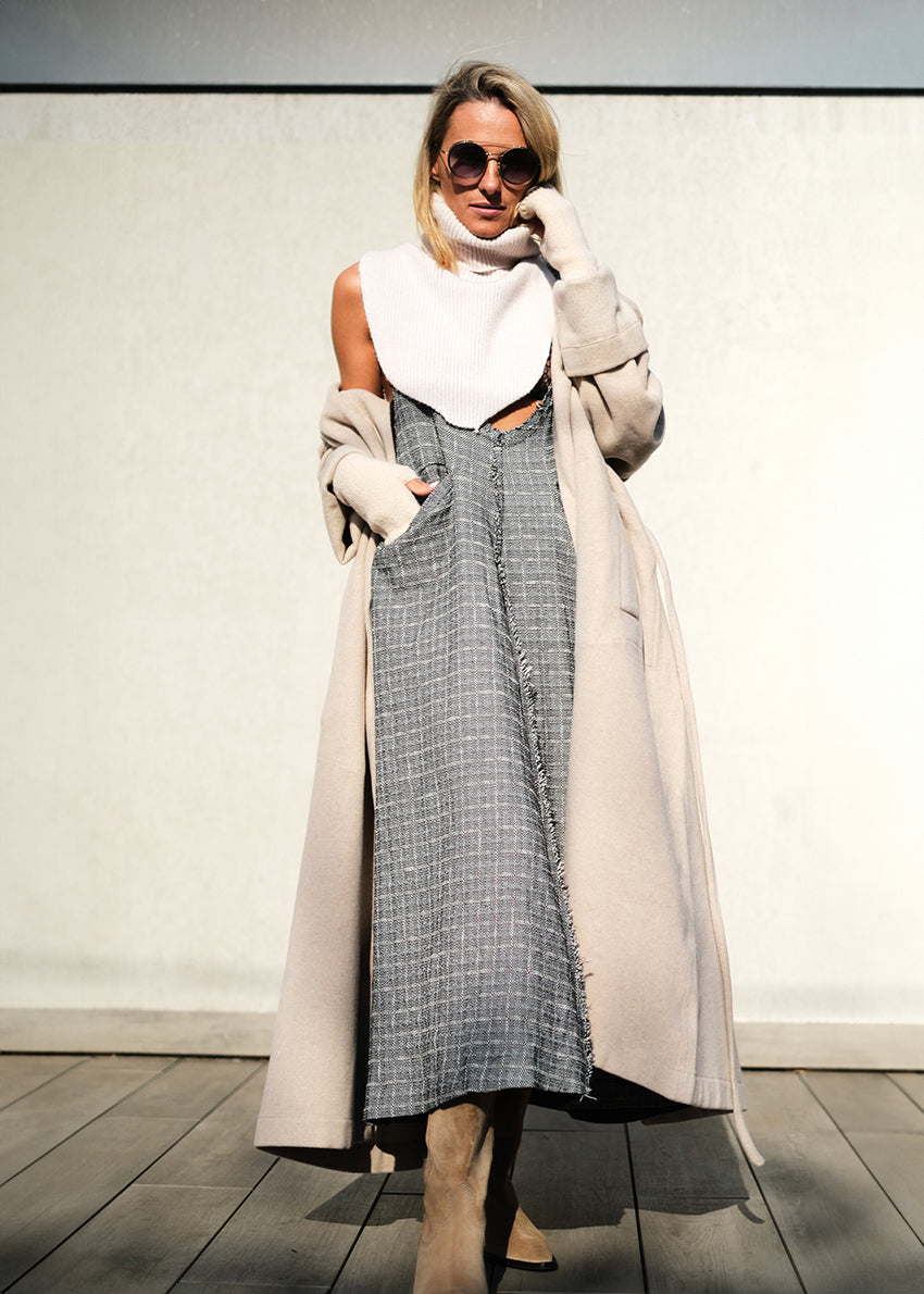 Woman wearing a beige wool coat with a grey dress and a white scarf