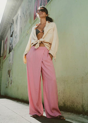 Woman wearing a beige shirt and pink pants standing against a light green wall.