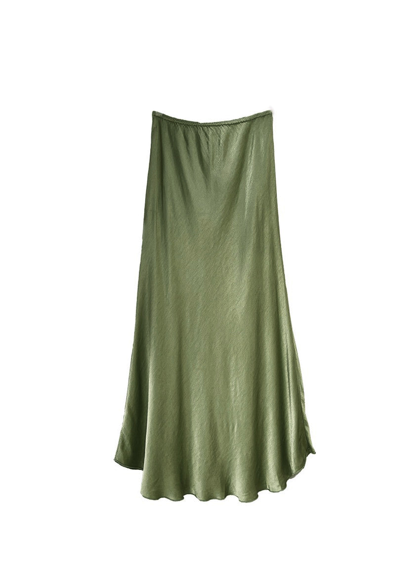 A person sitting on a chair wearing a beige tank top and a satin green khaki skirt 