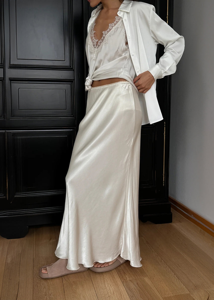 Person wearing a white satin skirt and top in a room with dark wooden furniture.