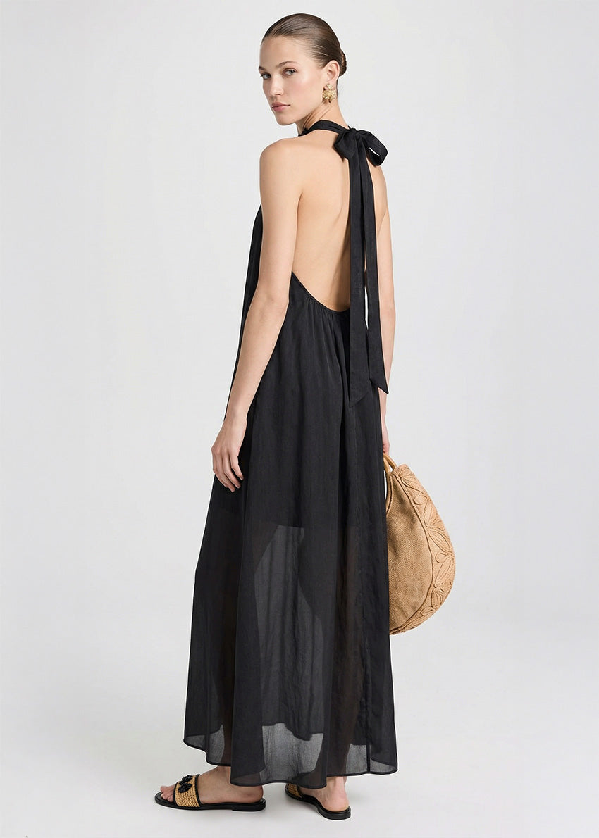 Woman wearing a black halter neck dress holding a beige bag against a plain background