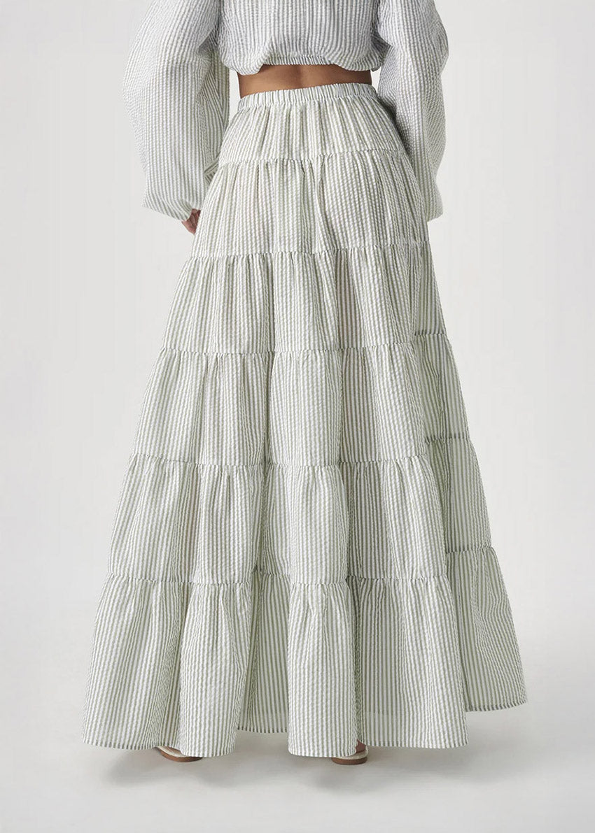 Woman wearing a tiered, long, white skirt with a plain background