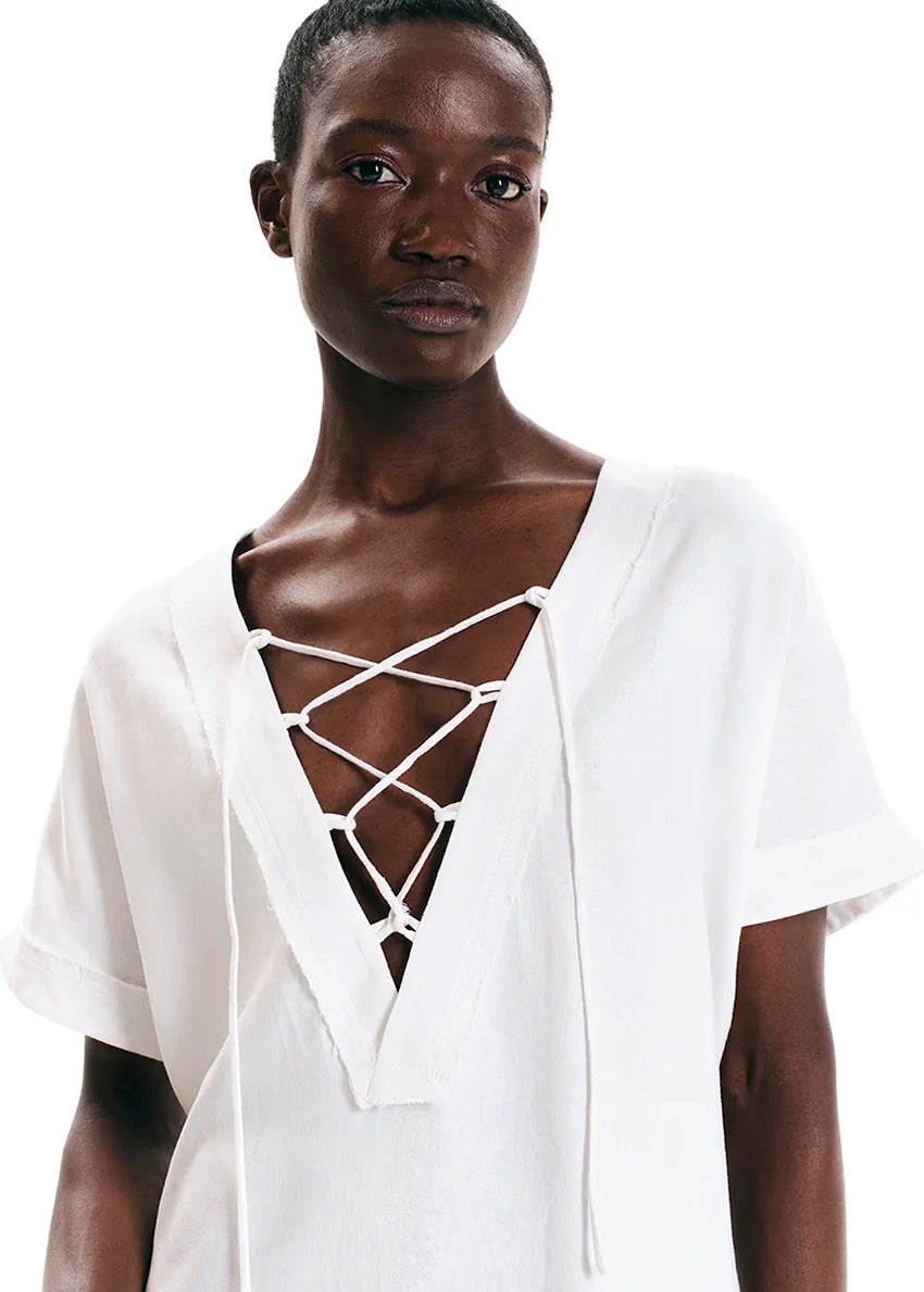 White tunic with front detail made of a linen and bamboo blend with a linen look.It has a boxy shape with short sleeves and mini length. It has a plunging “V” neck with ribbons that tie in “X” shapes while the fringes at the seams highlight its raw look.