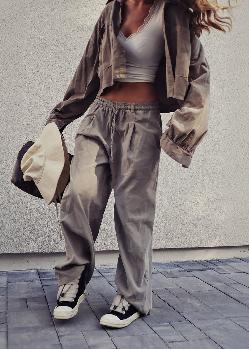 Person wearing a casual outfit with a jacket, pants, and sneakers against a plain background