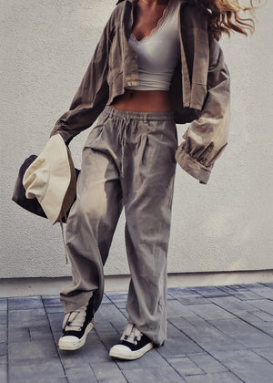 Person wearing a casual outfit with a jacket, pants, and sneakers against a plain background