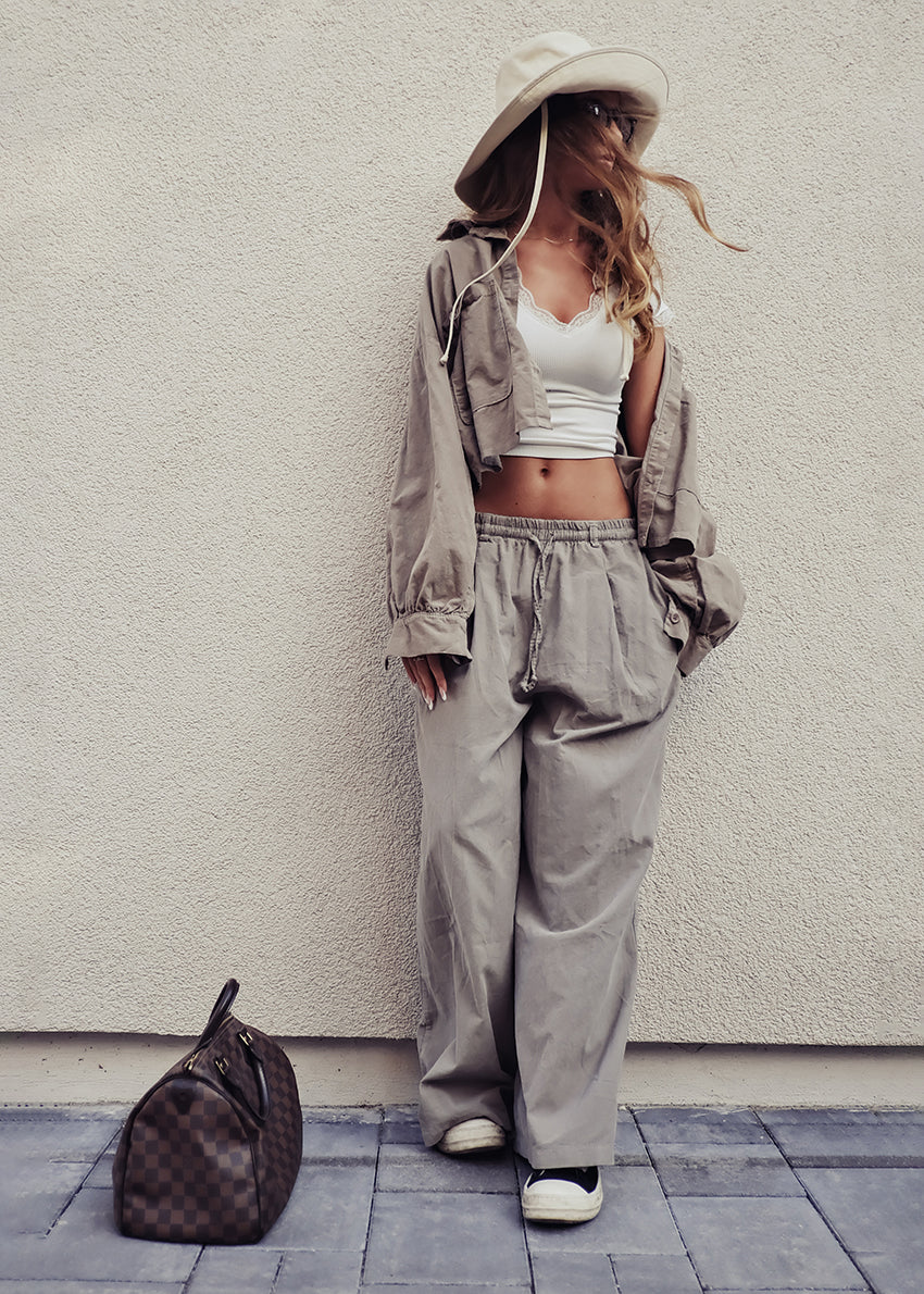 Person wearing a beige outfit with a white crop top and wide-leg pants, standing against a light gray wall.
