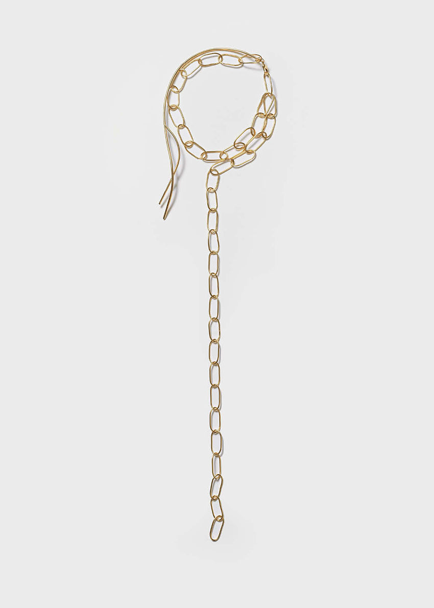 Gold chain necklace on a white strapless dress against a white background