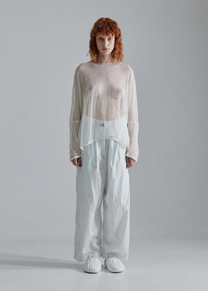Person wearing a layered outfit with a sheer top and light pants on a plain background