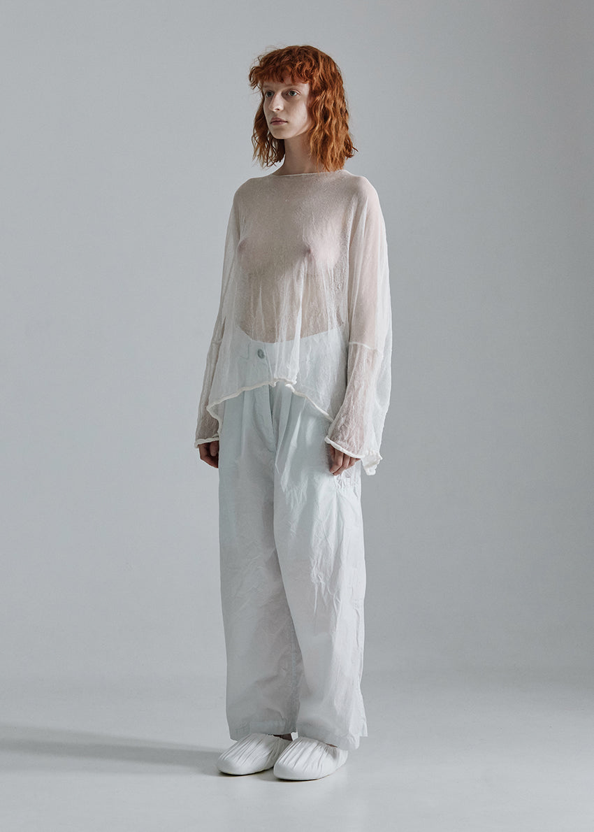 Person wearing a sheer white top and light gray pants on a plain background