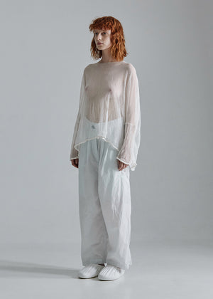 Person wearing a sheer white top and light gray pants on a plain background