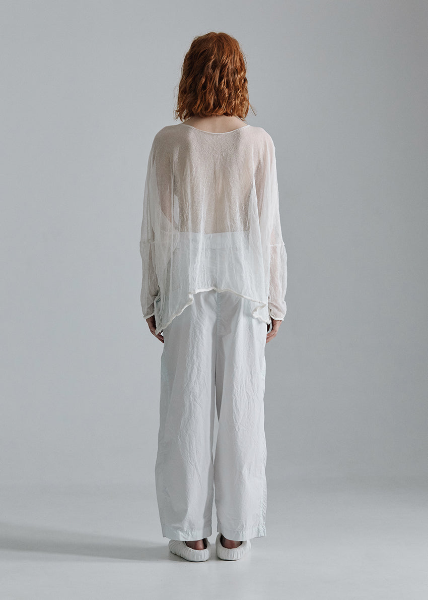 Person wearing a sheer white top and white pants against a gray background