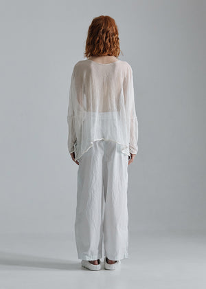 Person wearing a sheer white top and white pants against a gray background