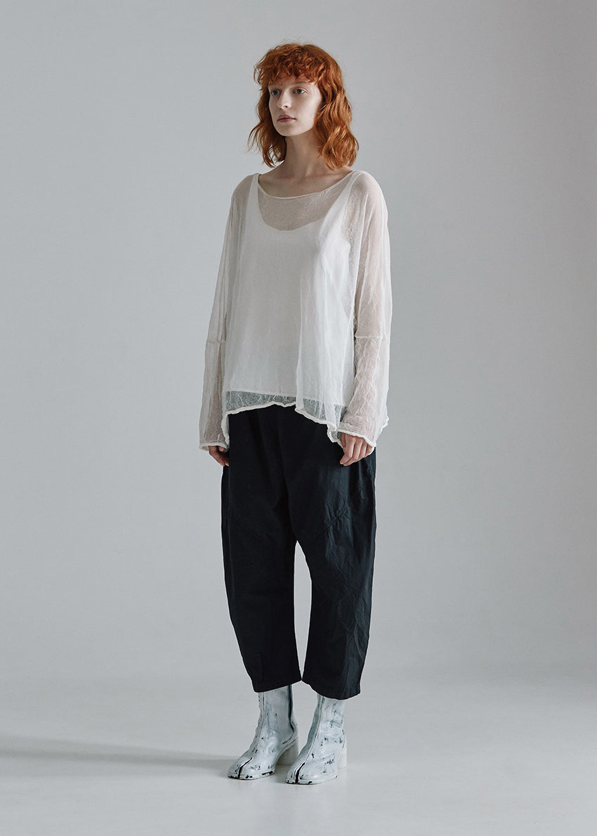 Person wearing a sheer white top and dark pants on a gray background