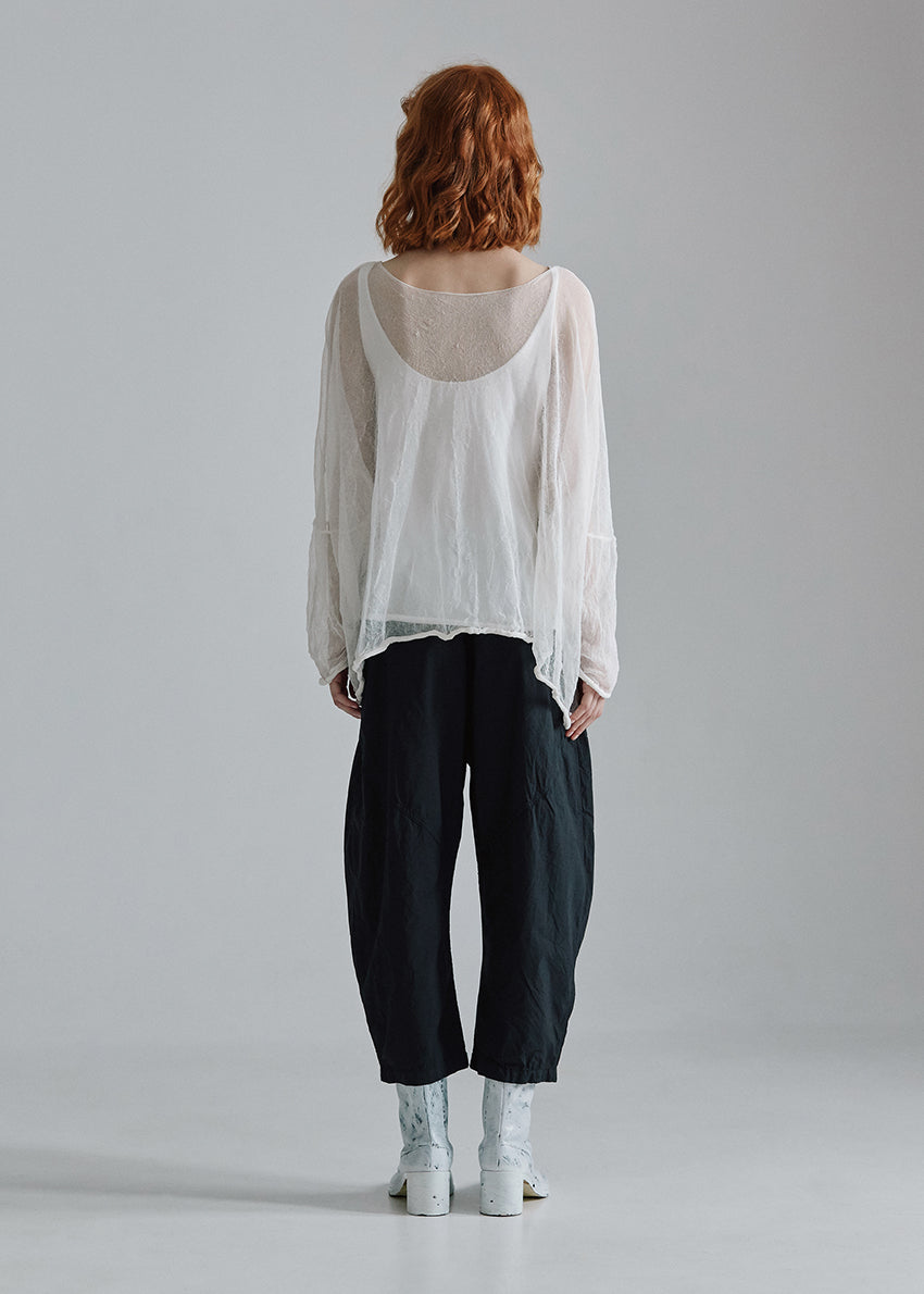Person wearing a white blouse and dark pants standing against a plain background